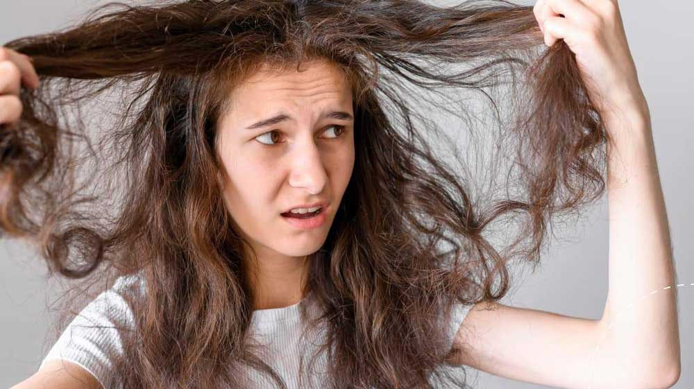 دختری با موهای خرمایی بلند در حالی که عصبانی است موهای خود را در دست گرفته و به سمت راست نگاه می کند - درمان ریزش مو در طب سنتی