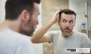 مردی که در آینه موهای خود را نگاه می کند و به موهای خود دست می کشد - عوارض کاشت مو